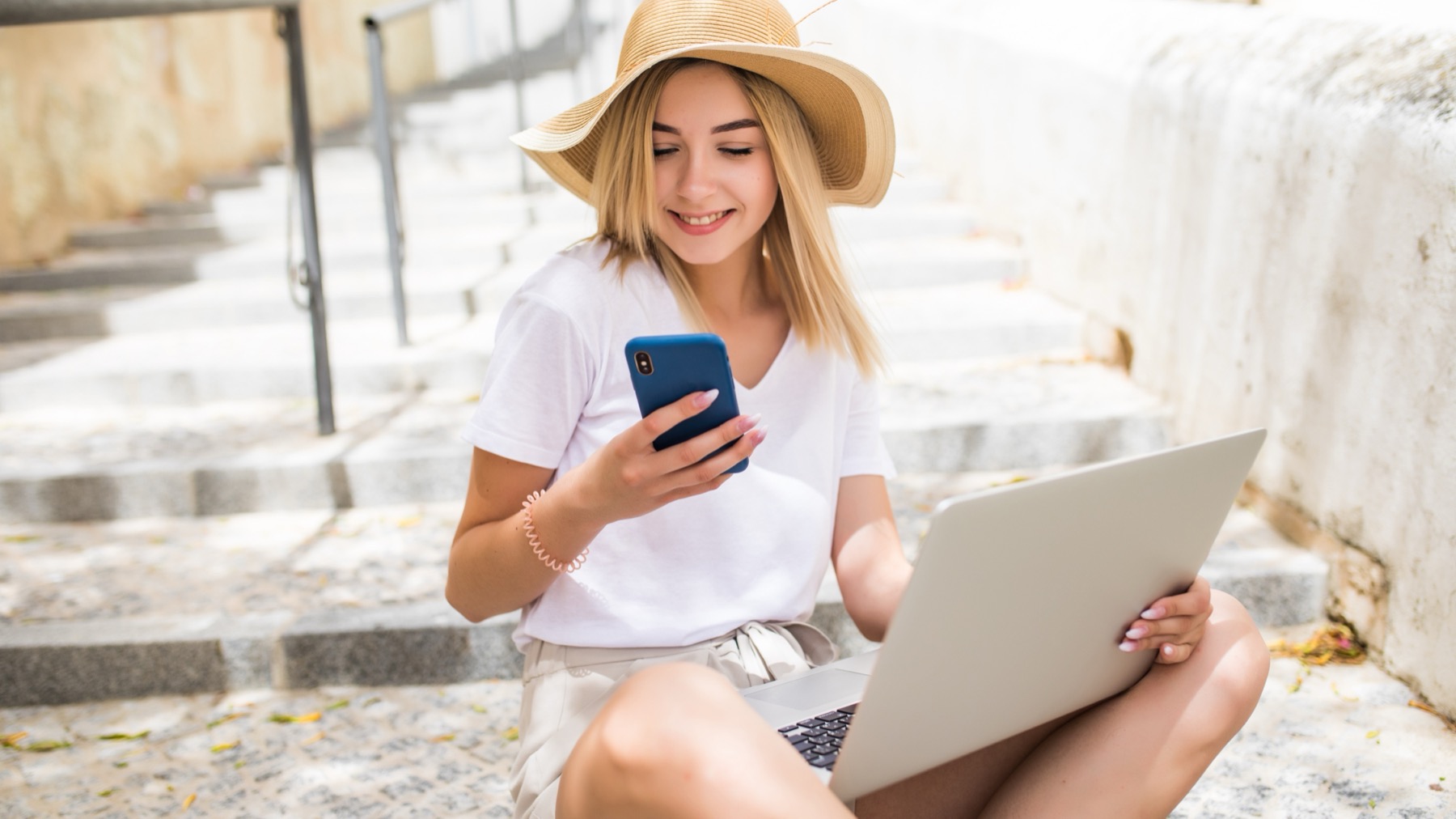 Traveler holding a phone next to an open laptop on city steps, illustrating whether an eSIM supports hotspot tethering
